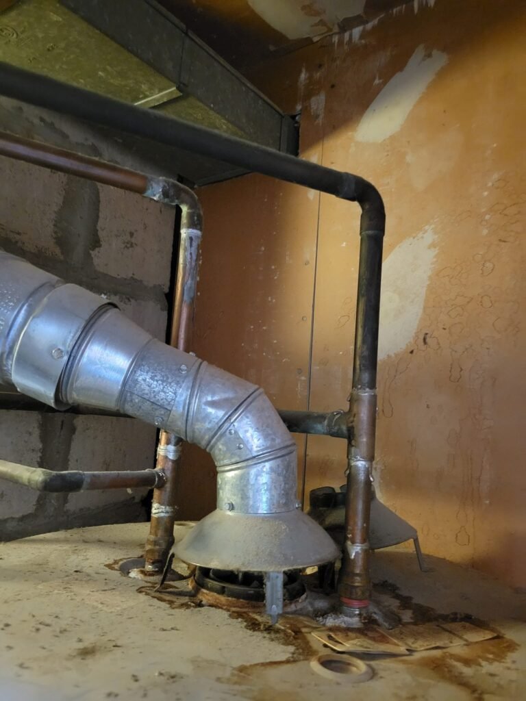Water heater flue vent and gas line in a basement before repair in Glenarden, MD